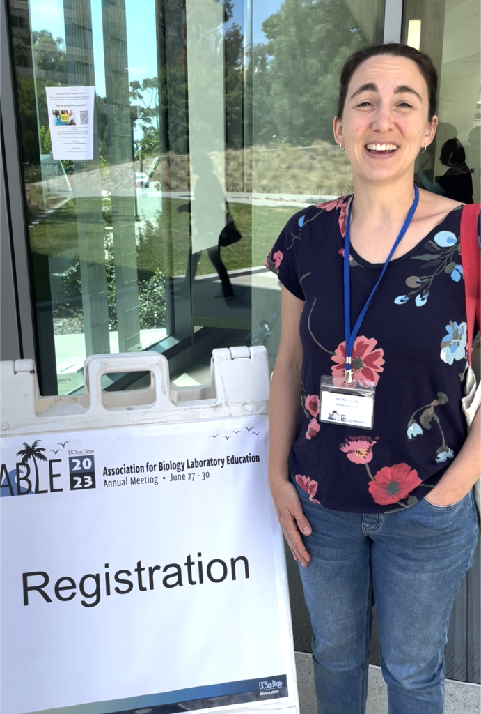 photo of Jen K at ABLE 2023 in front of a sandwich board that says "Registration"